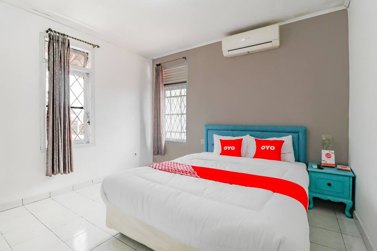 Quarto bem organizado com uma cama grande, cabeceira azul e mesa de cabeceira com um conjunto de almofadas vermelhas e brancas.