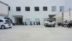 A parking area with several cars and motorcycles, a building with multiple windows and doors, and a concrete ground. - OYO 91455 New Hotelo (Jakarta)