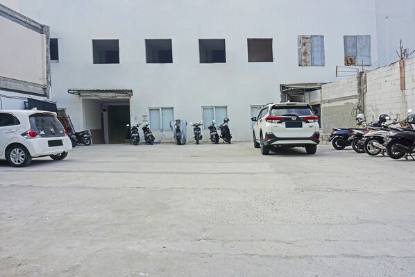 A parking area with several cars and motorcycles, a building with multiple windows and doors, and a concrete ground. - OYO 91455 New Hotelo (Jakarta)