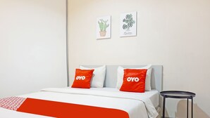 A hotel room with a bed, two pillows with "OYO" branding, a small black side table, and two wall art pieces depicting plants. - OYO 91455 New Hotelo (Jakarta)