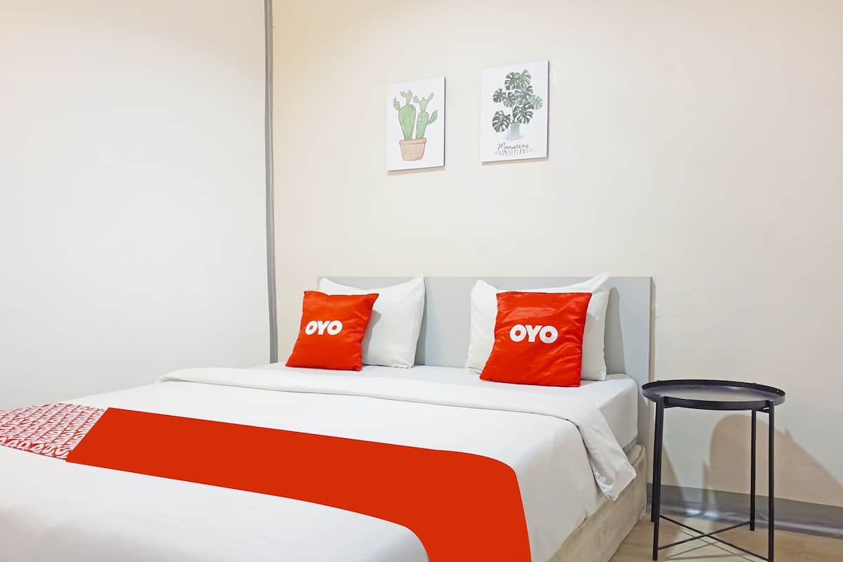 A hotel room with a bed, two pillows with "OYO" branding, a small black side table, and two wall art pieces depicting plants.