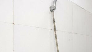 A shower with a flexible hose and a handheld showerhead mounted on a wall with white tiles. - OYO 91455 New Hotelo (Jakarta)