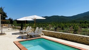 Una piscina con bordo piastrellato, circondata da un muro in pietra e qualche sedia a sdraio bianca.