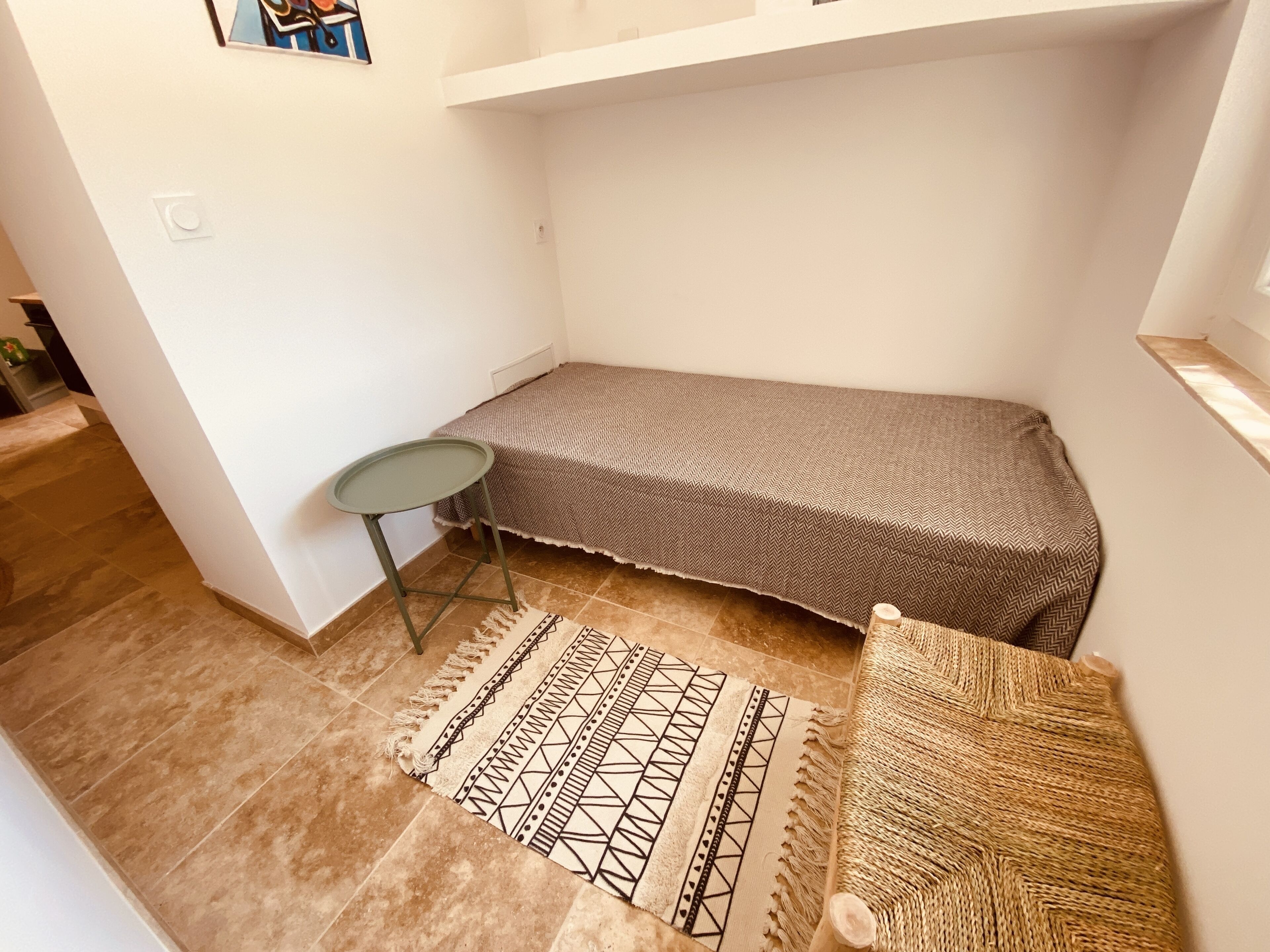 A small, compact room with a single bed, a small table, and a patterned rug.