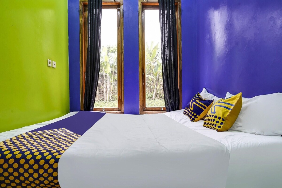 Ein Zimmer mit einem Bett, einem Vorhangfenster und Blick auf Grünflächen.