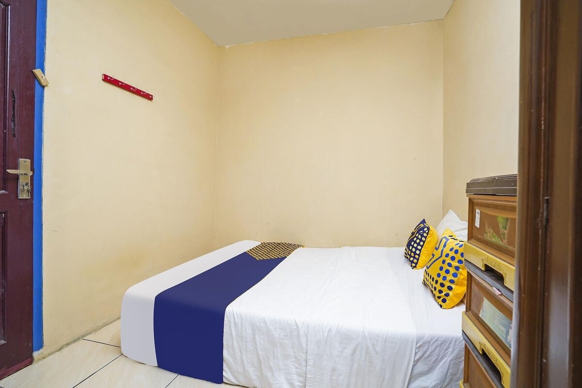 A small, single-bed room with a white bedspread, a blue accent, and patterned pillows.