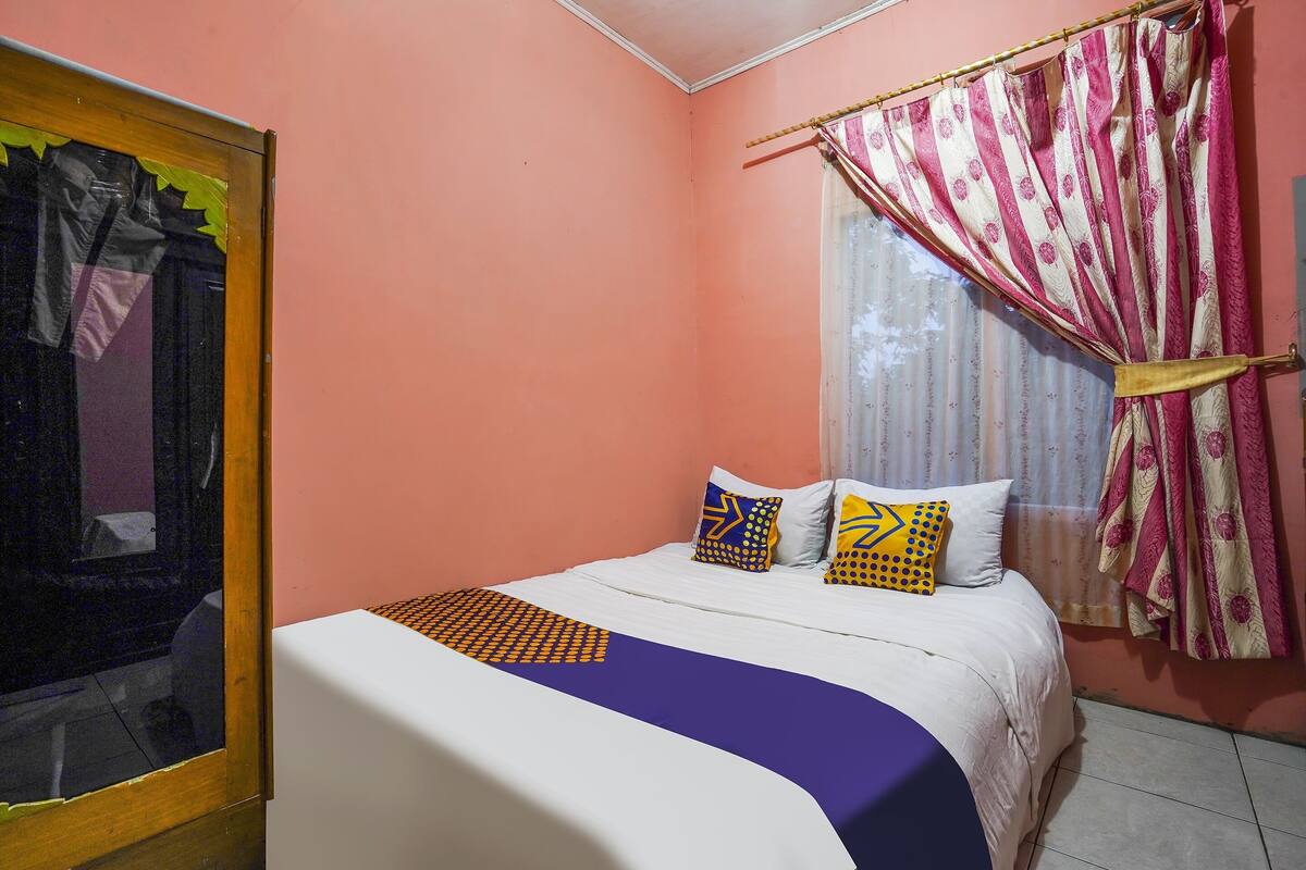 A bedroom with a bed, pillows, a window with curtains, and a mirror.