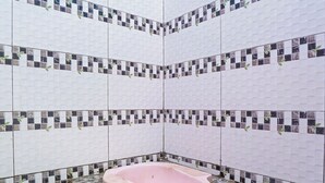 A bathroom with a stone floor, a pink bathtub, and tiled walls with a mosaic pattern. - OYO Homes 90916 Eco Tourism Geopark Rajamandala Homestay Syariah (Rajamandala Kulon)
