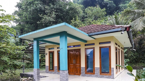 A two-story house with a tiled roof, a porch with blue pillars, and a large wooden door. - OYO Homes 90916 Eco Tourism Geopark Rajamandala Homestay Syariah (Rajamandala Kulon)