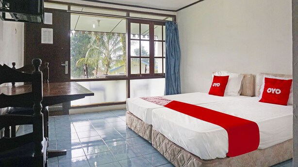 Una habitación de hotel con cama, escritorio, televisor y ventana con vista a palmeras.