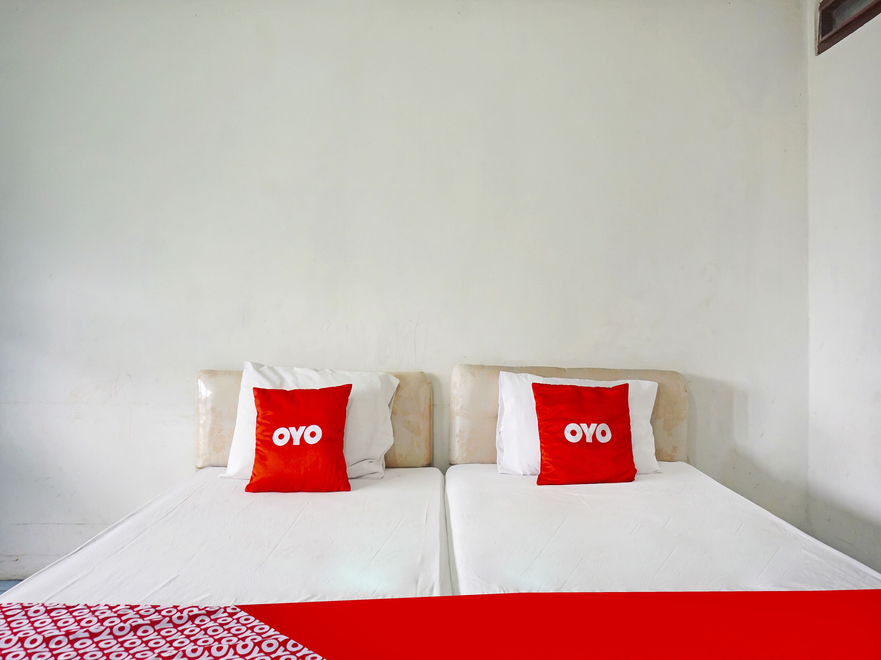 A double bed with white bedding and two red pillows with the word "OYO" on them.