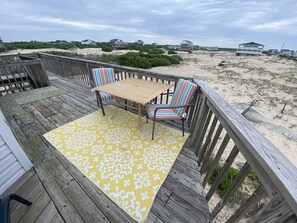A wooden deck with a yellow patterned rug, a wooden table, and striped chairs. - Gorgeous 6BR house, Wild Horses, stunning views! Private parking. 4WD required. (Corolla)