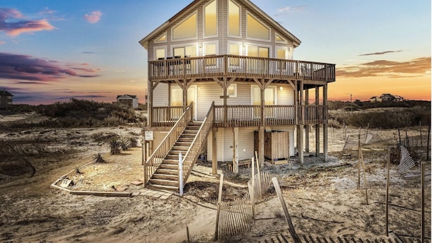 A wooden beach house with a balcony and stairs leading to the entrance.