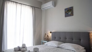 Un dormitorio con cama, toallas, aire acondicionado, una mesita de noche y un cuadro en la pared.