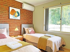 A hotel room with two beds, a brick wall, a window with curtains, and a framed picture on the wall.