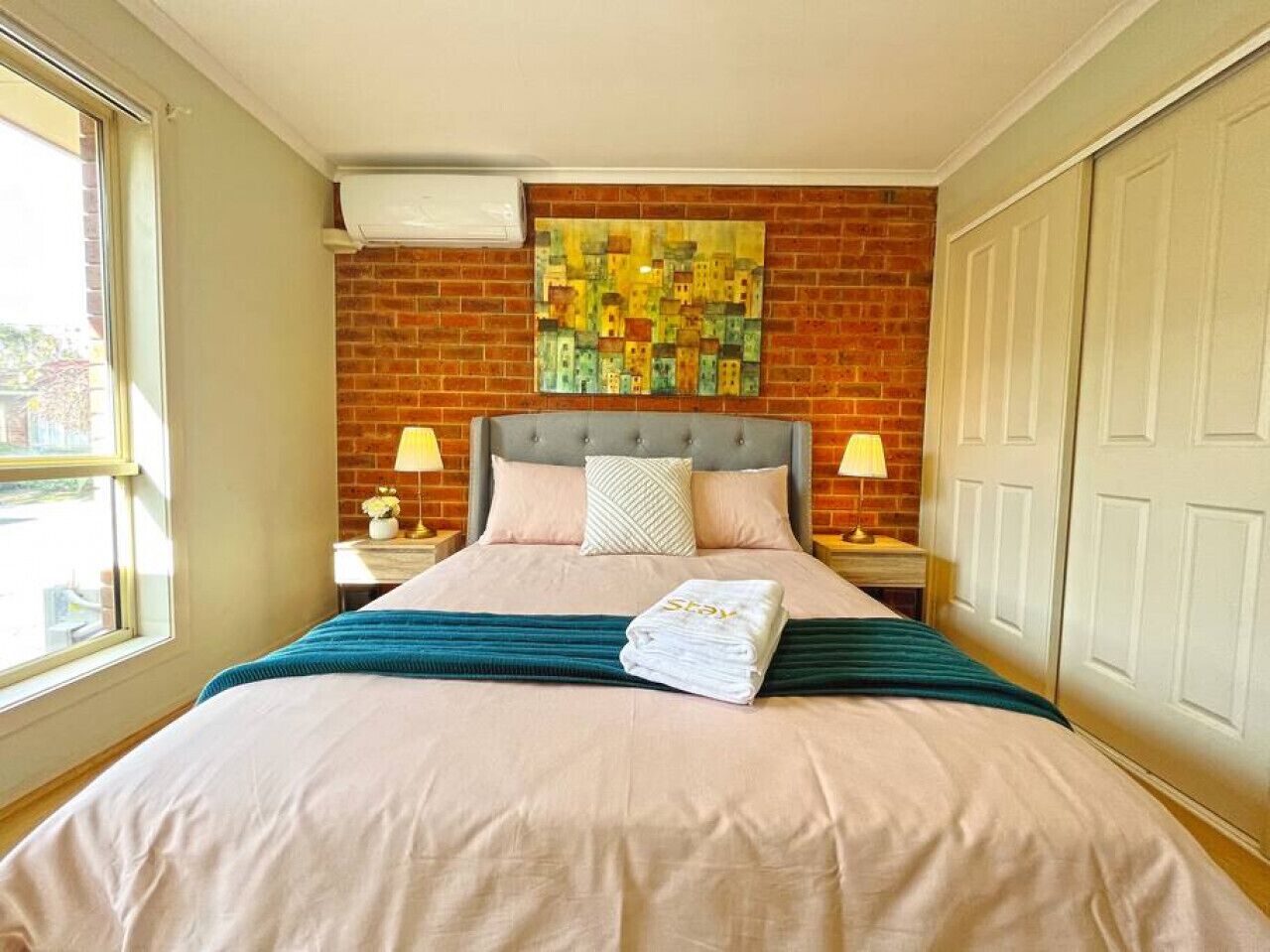 A hotel room with a bed, a brick wall, a painting, and a wardrobe.