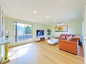 A spacious living room with a large window, a flat-screen TV, a sofa, and a coffee table.