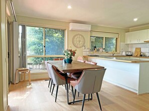 A modern kitchen with a dining area, large windows, and a clock on the wall.
