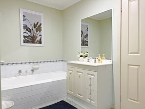 A bathroom with a white bathtub, a sink with a mirror, and cabinets.