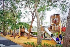 A playground with slides and climbing structures surrounded by trees.