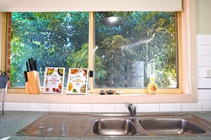 A kitchen with a window, stainless steel sink, and two cookbooks on the windowsill.