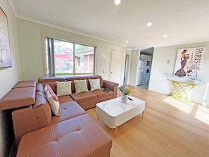 A modern living room with a brown leather sofa, a white coffee table, and a glass-top table with a yellow base.