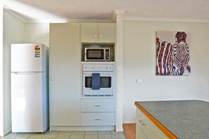 A kitchen with a refrigerator, microwave, oven, and a painting on the wall.