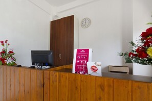 A reception desk with a computer, a clock, and a poster. - Hotel O Forrest’inn (Kediri)