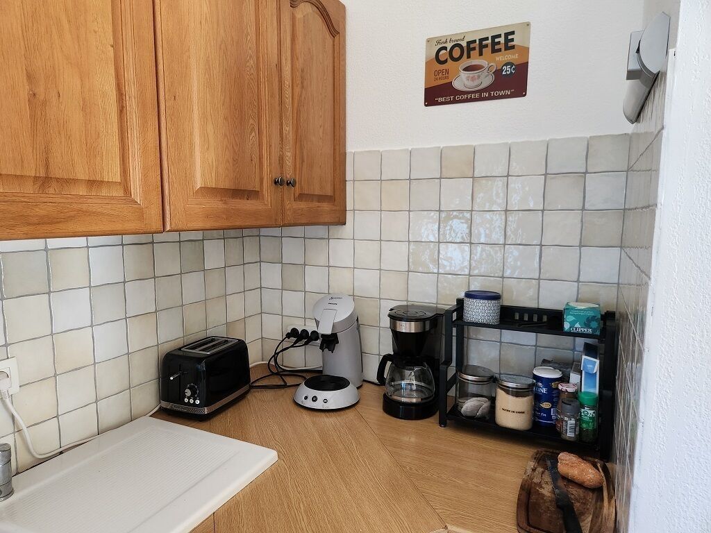 A kitchen with wooden cabinets, a coffee machine, a toaster, and a shelf with jars and a bread loaf.