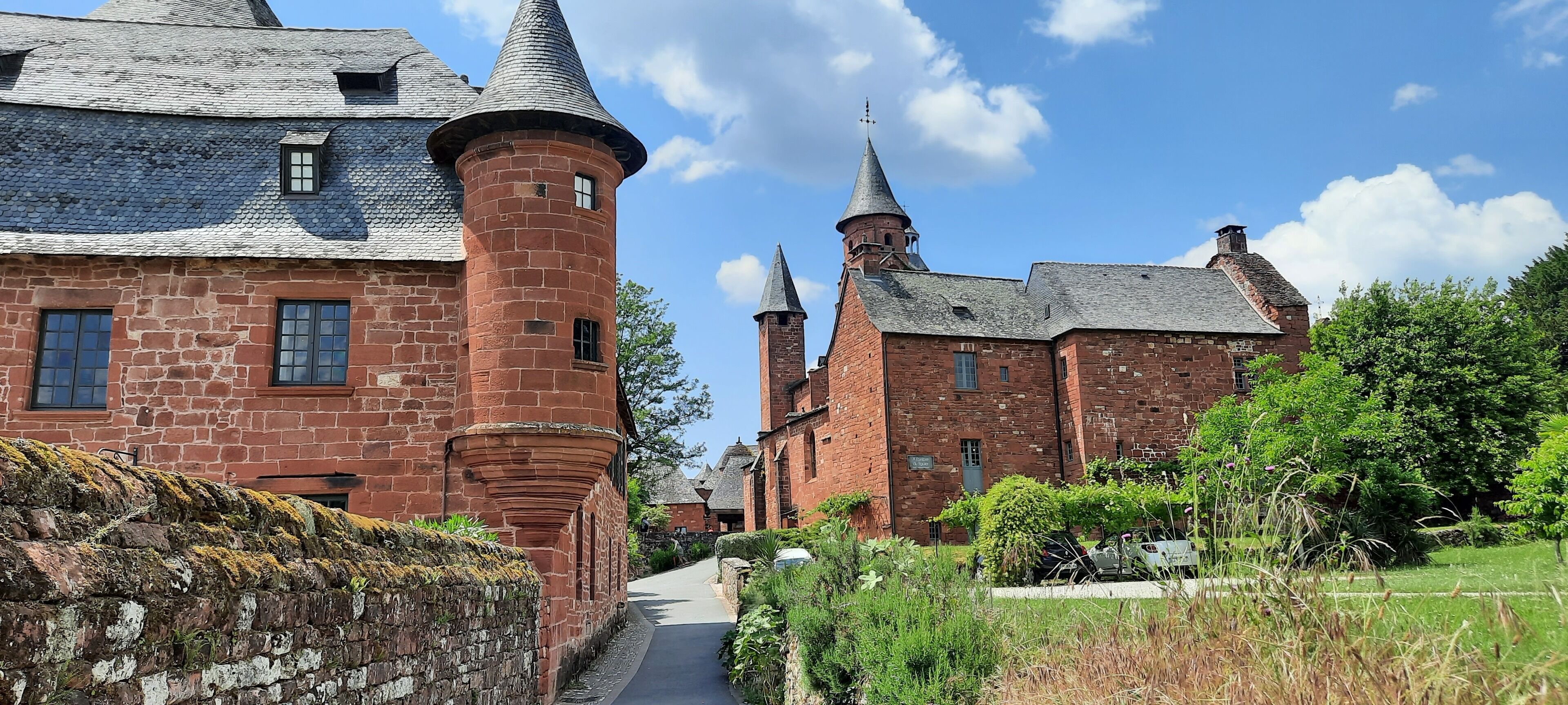 Um edifício histórico com uma torre imponente e várias torres, rodeado por vegetação exuberante e um céu claro.