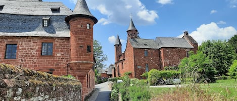 Un edificio histórico con una torre destacada y múltiples agujas, rodeado de abundante vegetación y un cielo despejado.