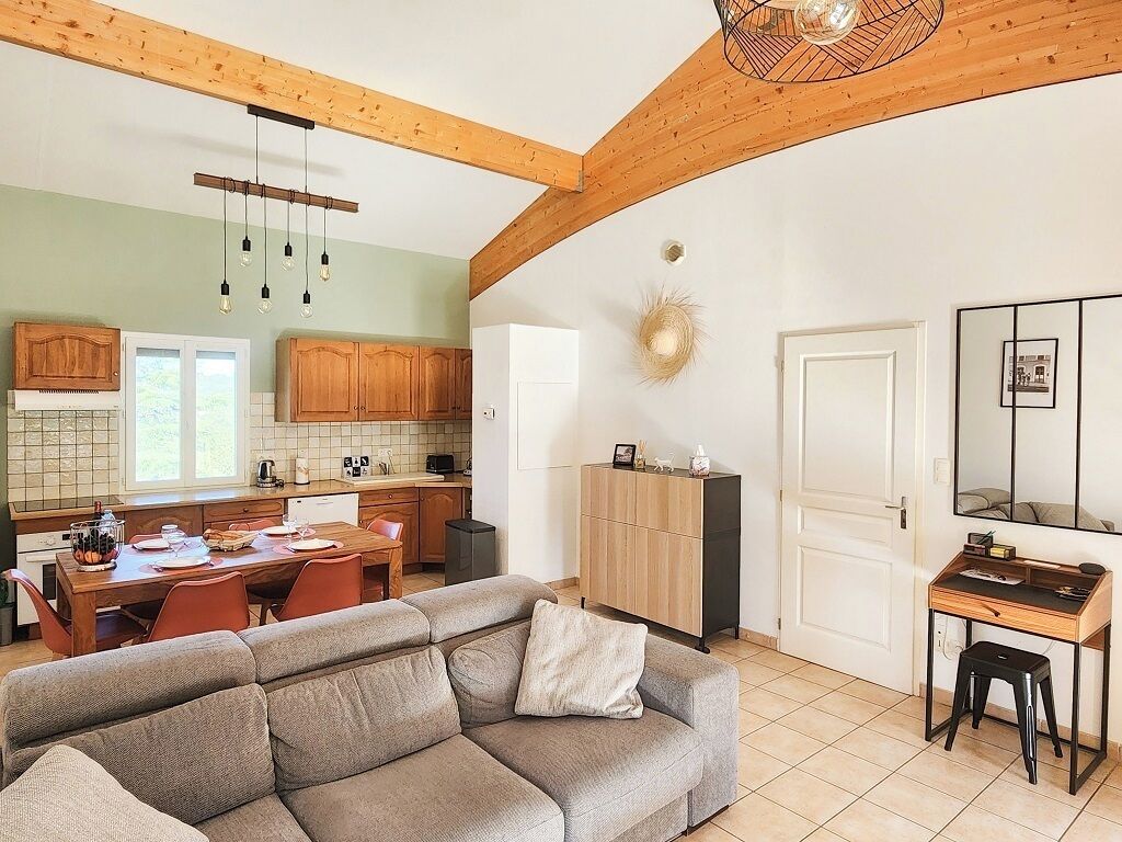 A modern kitchen with wooden cabinets, a dining area with a table and chairs, a sofa, and a desk with a chair.