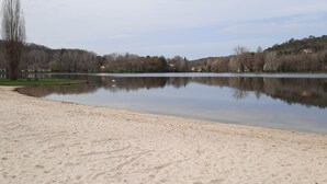 Une plage de sable fin, avec un lac paisible, des arbres et des maisons en arrière-plan.