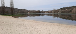 Een zandstrand met een rustig meer, bomen en huizen op de achtergrond.