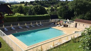 Une piscine rectangulaire avec une terrasse en bois et une clôture blanche. Des chaises longues et des parasols sont disposés le long du bord de la piscine.