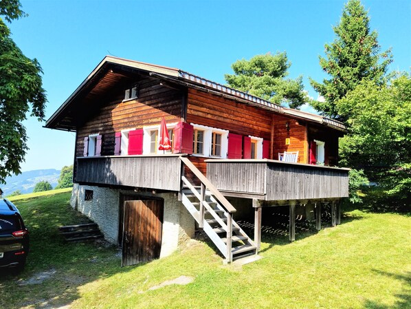 A wooden chalet with a balcony, a staircase, and a stone foundation.