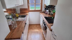 Eine kompakte Küche mit weißen Schränken, einer Holz Arbeitsplatte, einem Fenster und Blick ins Freie.