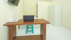 A small room with a wooden desk, a laptop, a teal stool, a white door, and a TV mounted on the wall. - OYO 91635 Wisma Terace House (Jakarta)