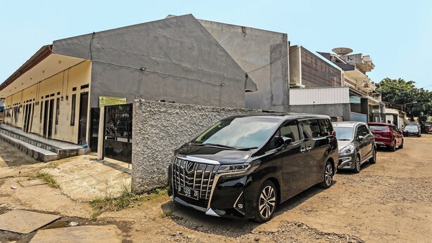 A black minivan parked in front of a building with a stone facade and a metal roof. - OYO 91635 Wisma Terace House (Jakarta)