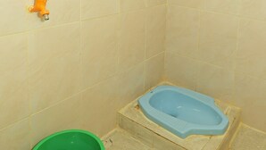 A bathroom with a bathtub, a green bucket, and an orange faucet. - OYO 91635 Wisma Terace House (Jakarta)