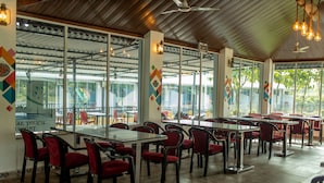 A spacious indoor dining area with multiple tables and red chairs, large windows, and a wooden ceiling. - Canal Touch Resort (Karjat)