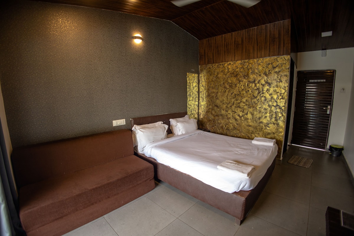 A bedroom with a bed, a brown sofa, a wall-mounted light, and a door.