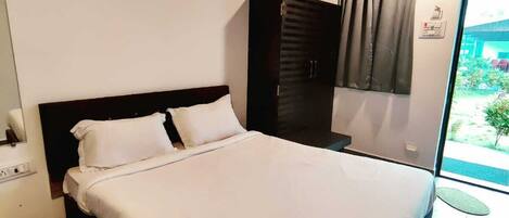 Une chambre à coucher comprenant un lit, une armoire, un appareil de climatisation, un ventilateur de plafond et une fenêtre avec des rideaux.