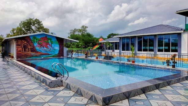 A swimming pool with a mural, a covered area with windows, and a tiled walkway. - Canal Touch Resort (Karjat)