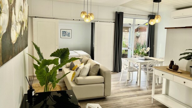 A modern living room with a sofa, a dining table, and a kitchen area.