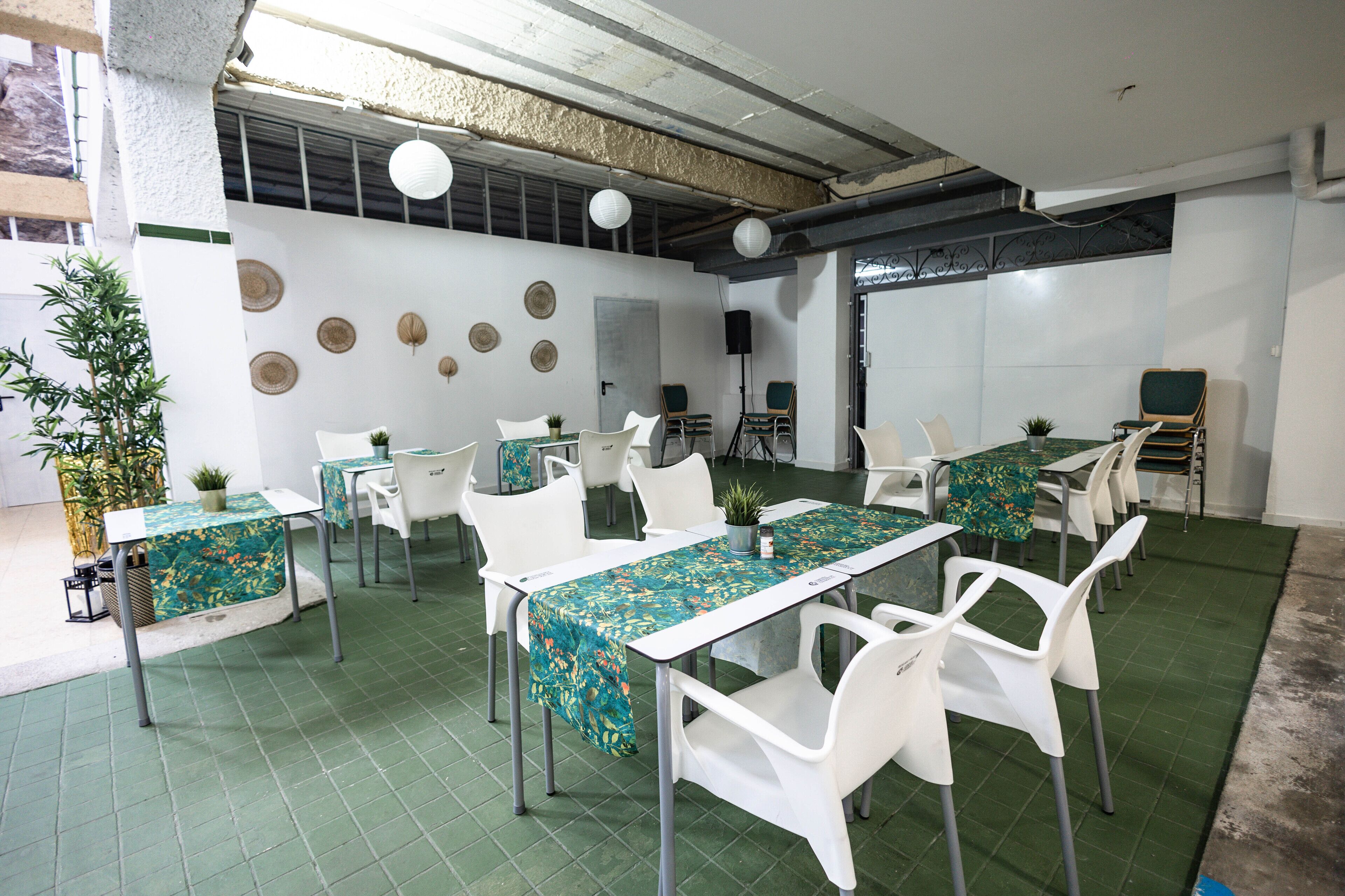 Un salón de conferencias con sillas y mesas blancas, suelo verde y paneles decorativos en la pared.