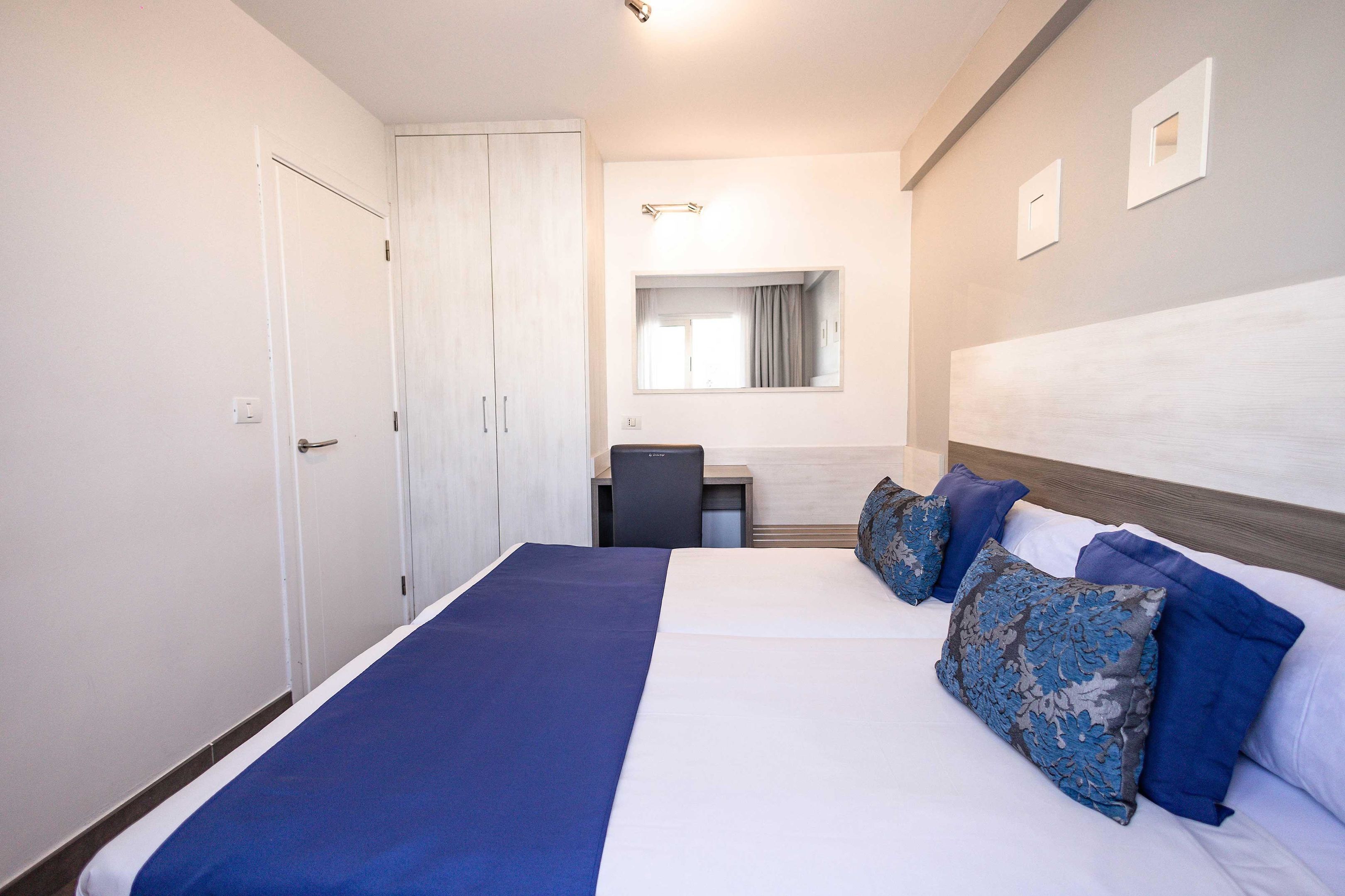 Una habitación de hotel con cama, escritorio, silla y armario.