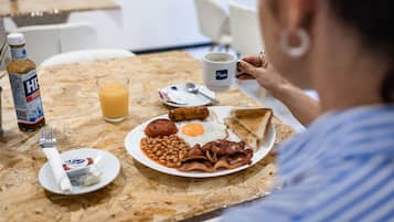 Une assiette de petit-déjeuner comprenant des œufs, du bacon, des haricots, des toasts et un verre de jus d’orange.