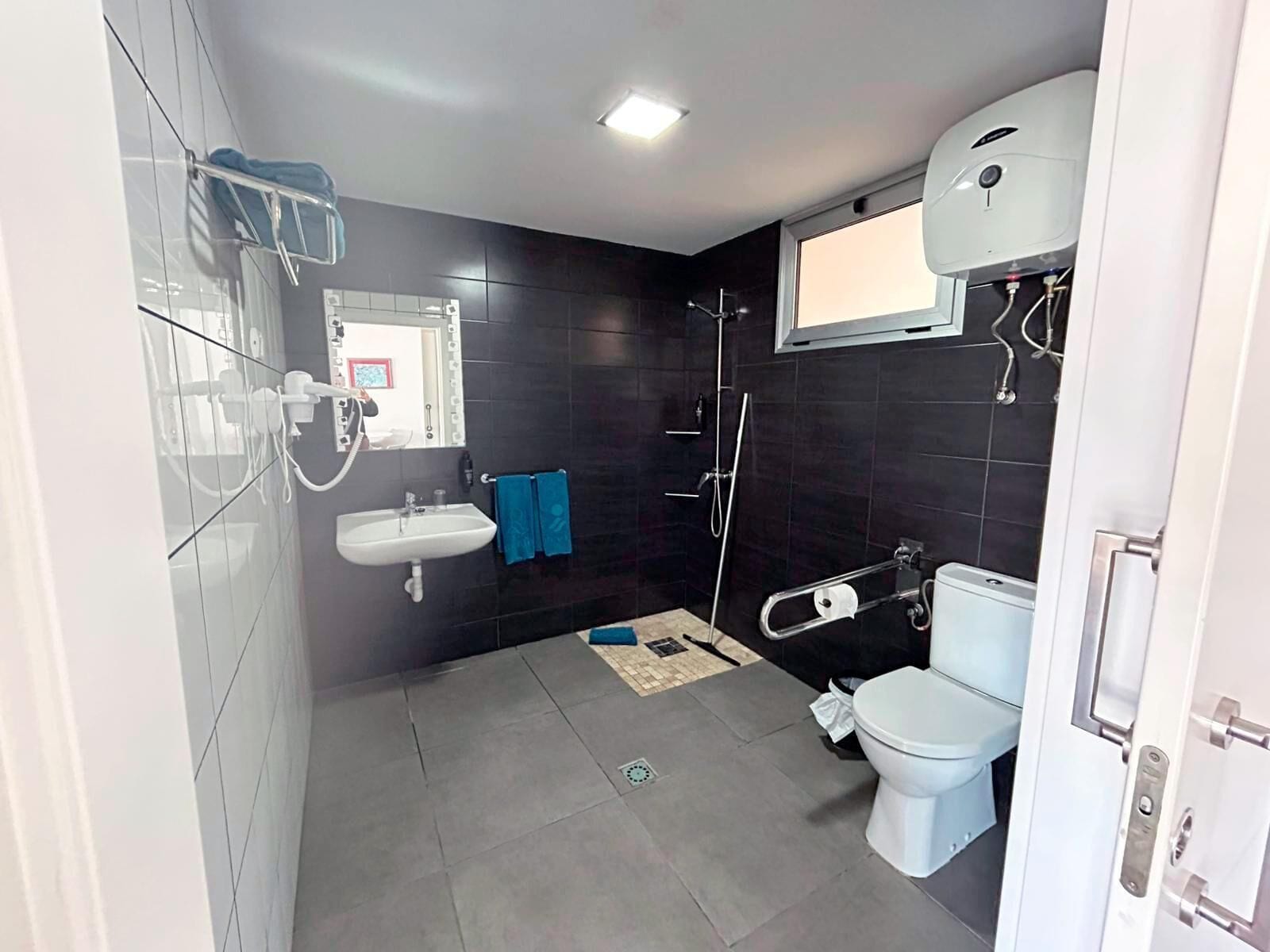 A modern bathroom with a shower, toilet, sink, and a window above the toilet.