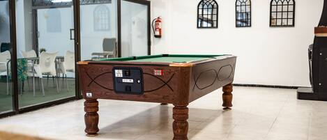 Une table de billard dans une pièce aux murs blancs, avec un extincteur et une fenêtre donnant sur un paysage.